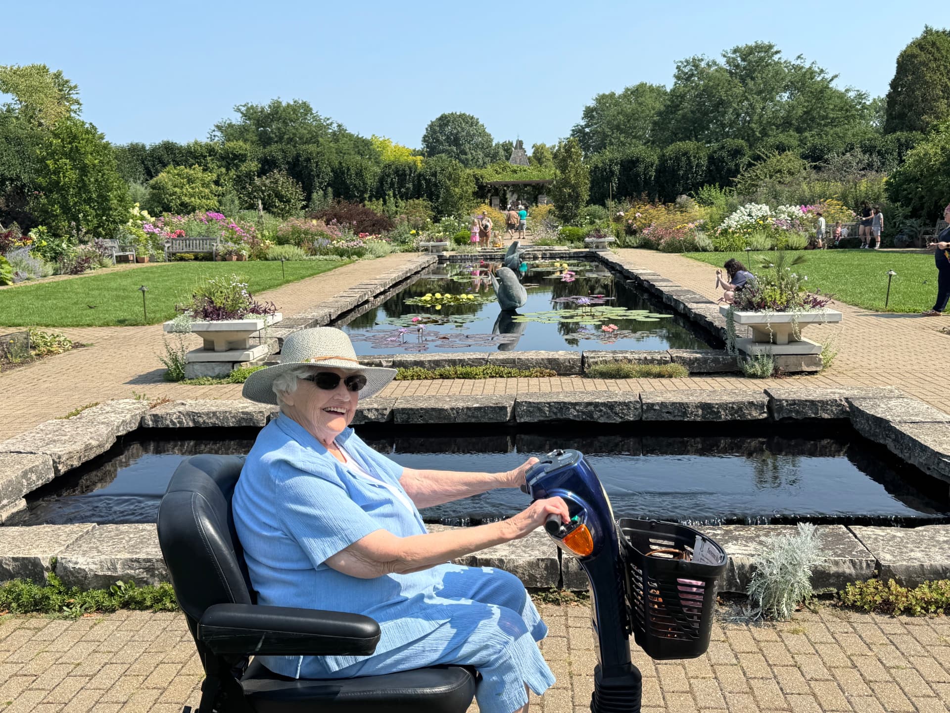 A smiling Caring Companion client on a mobility scooter enjoying a sunny garden outing