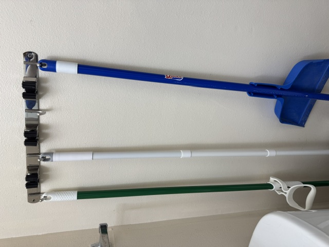 Brooms and a dustpan neatly organized on a wall-mounted rack installed during a special project visit