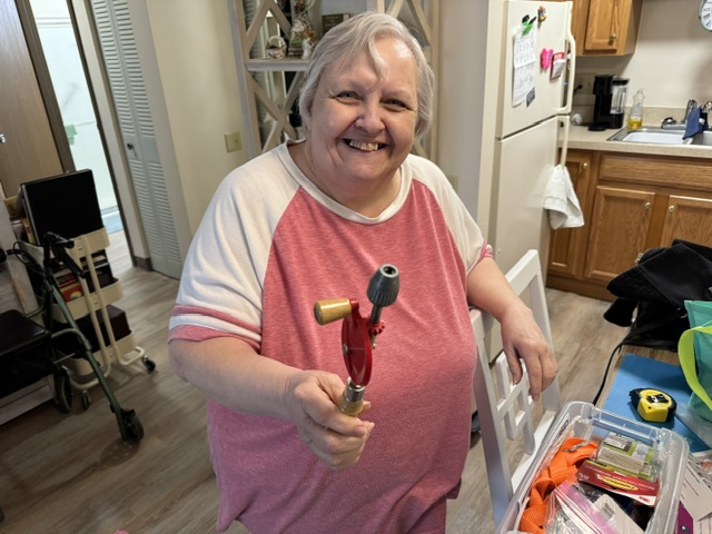A smiling Caring Companion client holding a small hand drill during a special project visit